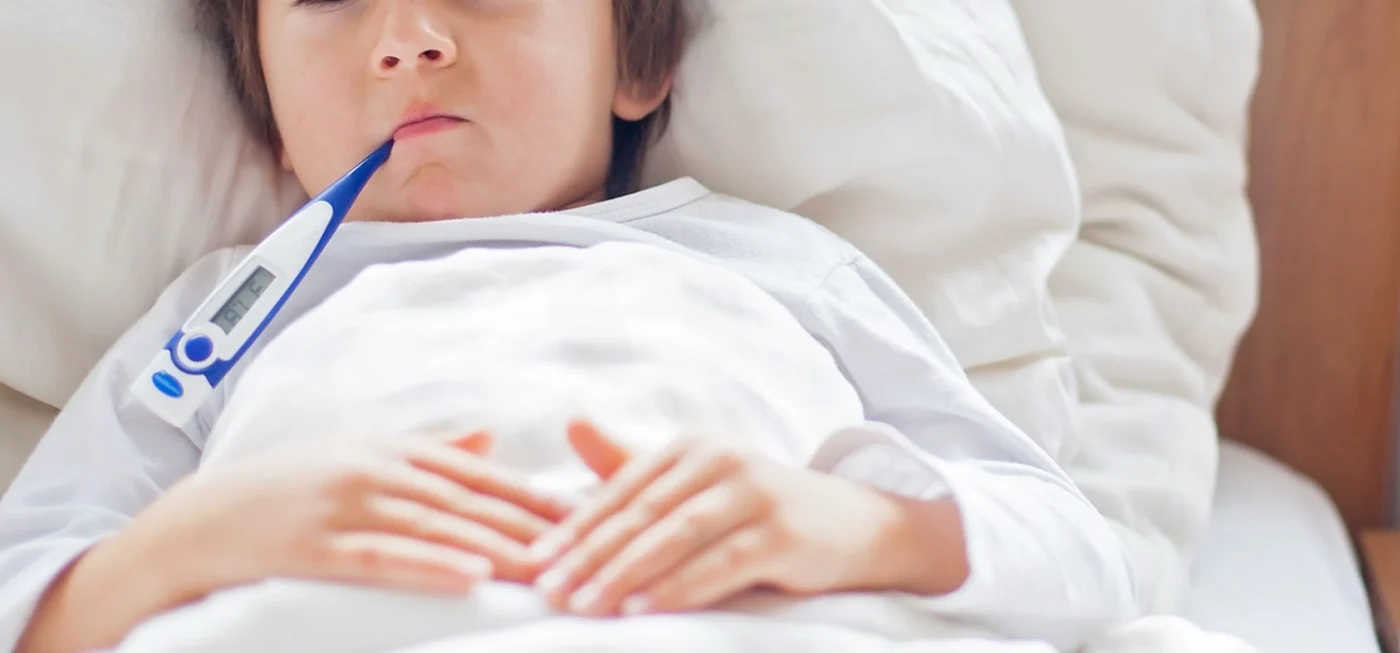Comment choisir son thermomètre frontal : Le guide d'achat complet 2024 23 Enfant allongé dans un lit avec un thermomètre électronique dans la bouche, visiblement fiévreux.