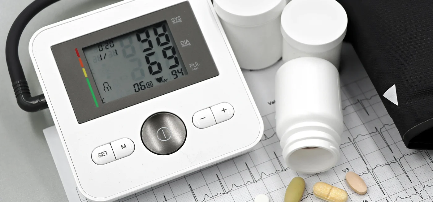 Tensiomètre électronique ou manuel : lequel est fait pour vous ? 2 Tensiomètre électronique affichant une mesure de la tension artérielle, entouré de pilules, flacons et tracé ECG sur fond médical.