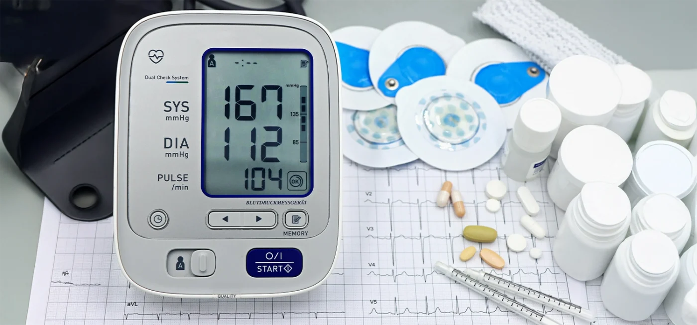 Comment utiliser un tensiomètre correctement pour des résultats fiables ? 2 Gros plan sur un tensiomètre numérique affichant une tension artérielle élevée, entouré de médicaments et d’accessoires médicaux.