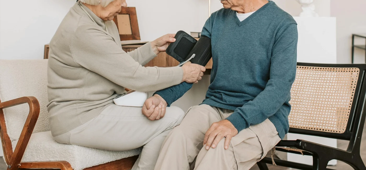Comment utiliser un tensiomètre correctement pour des résultats fiables ? 13 Une femme aide un homme âgé à installer un brassard de tensiomètre pour prendre sa tension à domicile.