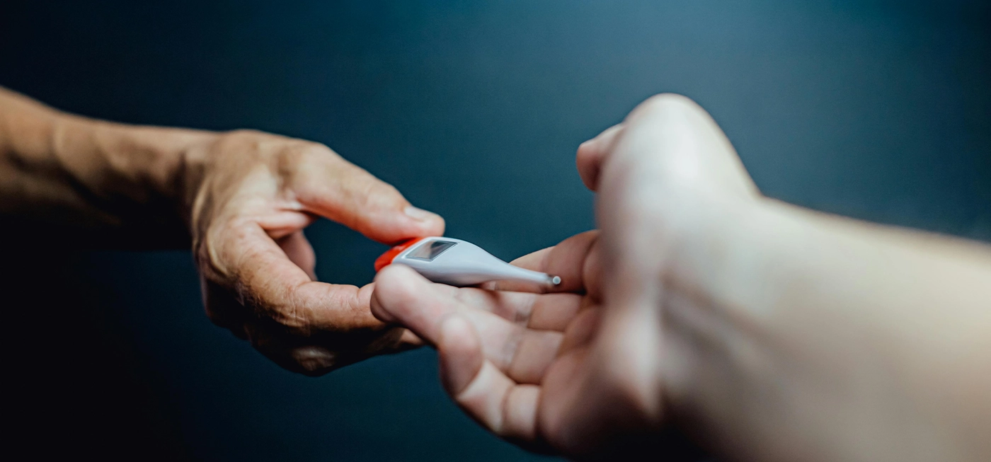 Comment bien choisir son matériel médical en 2025 ? Le guide expert. 2 Deux personnes se transmettent un thermomètre électronique, illustrant l’utilisation de matériel médical pour surveiller la santé au quotidien.
