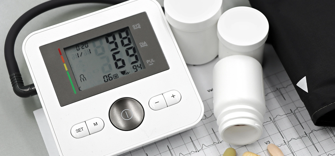 Matériel Médical en Ligne : Produits de Santé, Accessoires et Équipements de Qualité à Prix Pas Cher 2 Tensiomètre électronique affichant une mesure de tension artérielle, accompagné de flacons de médicaments et de comprimés posés sur un électrocardiogramme.